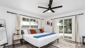 Ein Schlafzimmer mit Bett, Nachttischen, Deckenventilator und großen Fenstern.