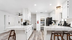 Eine moderne Küche mit weißen Schränken, einer großen Kochinsel mit Barhocker und einem Deckenventilator.