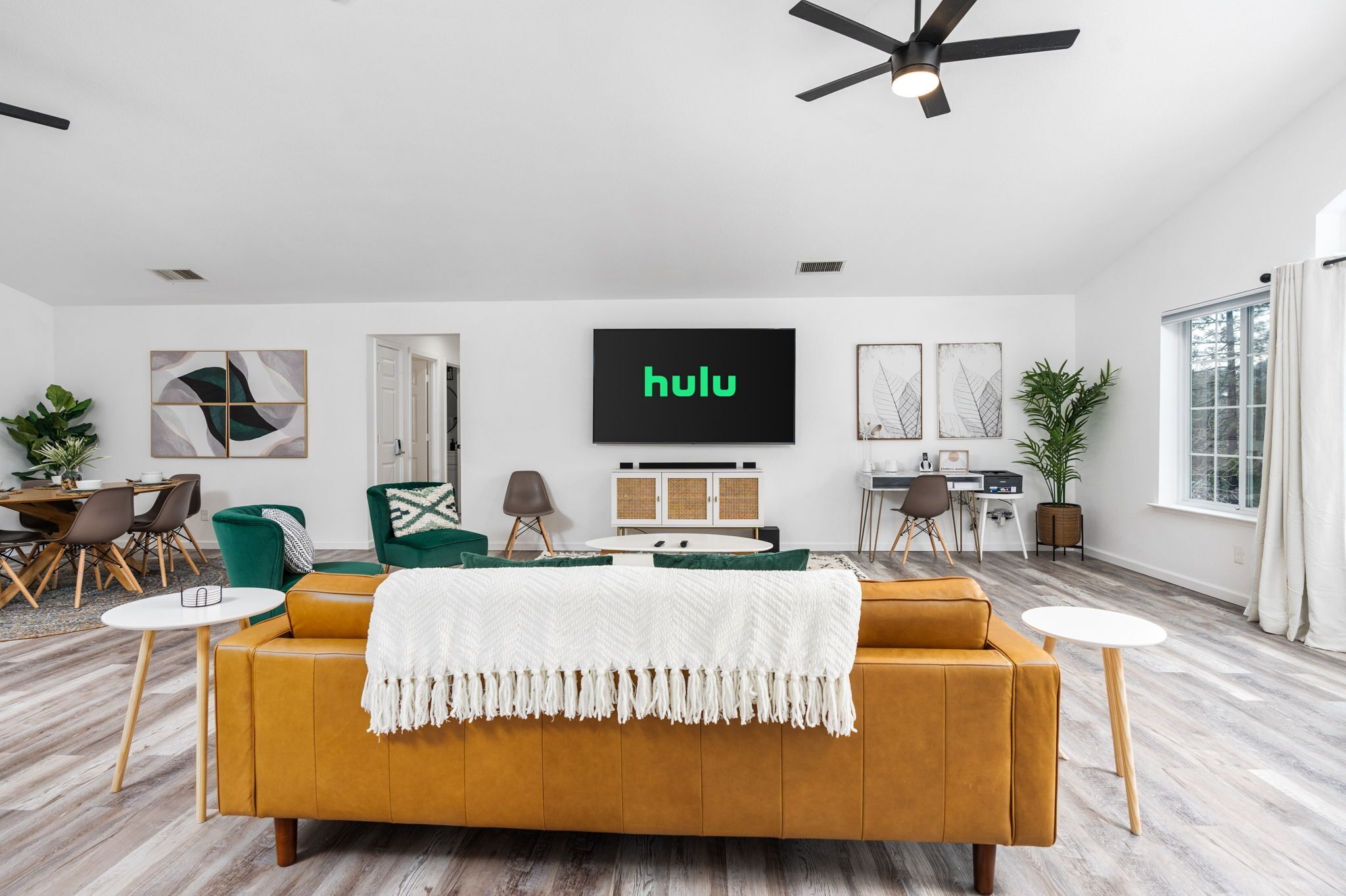 Een moderne woonkamer met een grote bank, een televisie waarop 'hulu' wordt weergegeven, en een eethoek met stoelen en een tafel.