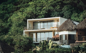 A modern two-story building with a balcony, surrounded by lush greenery.
