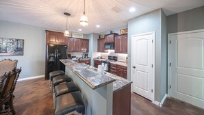A modern kitchen with a central island, bar stools, wooden cabinets, and pendant lighting. - Right At Home-Midland Monterrey House (Midland)