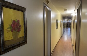 A hotel hallway with framed artwork on the walls, doors leading to rooms, and a wooden floor. - Restwell Motel Moncton (Berry Mills)