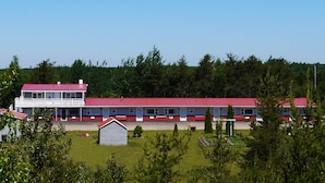 Um motel com telhado vermelho e fachada branca, vários quartos e um pequeno galpão no jardim da frente.