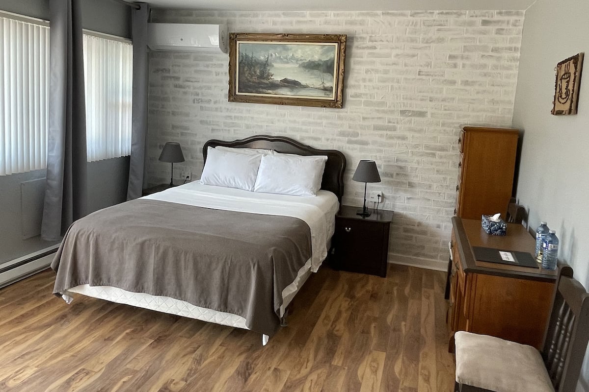 A bedroom with a bed, bedside tables, a dresser, and a painting on the wall.