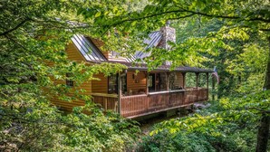 A log cabin with a porch, surrounded by dense forest. - WindFall-Stunning, Pet Friendly, Creekside Cabin (Maggie Valley)