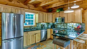 A kitchen with wooden cabinets, stainless steel appliances, a stone backsplash, and a window. - WindFall-Stunning, Pet Friendly, Creekside Cabin (Maggie Valley)