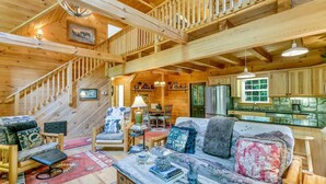 A cozy log cabin interior with a staircase, wooden furniture, a dining area, and a kitchen. - WindFall-Stunning, Pet Friendly, Creekside Cabin (Maggie Valley)