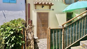 Una stretta scala conduce a una porta di legno, una recinzione di bambù e un ombrello verde.