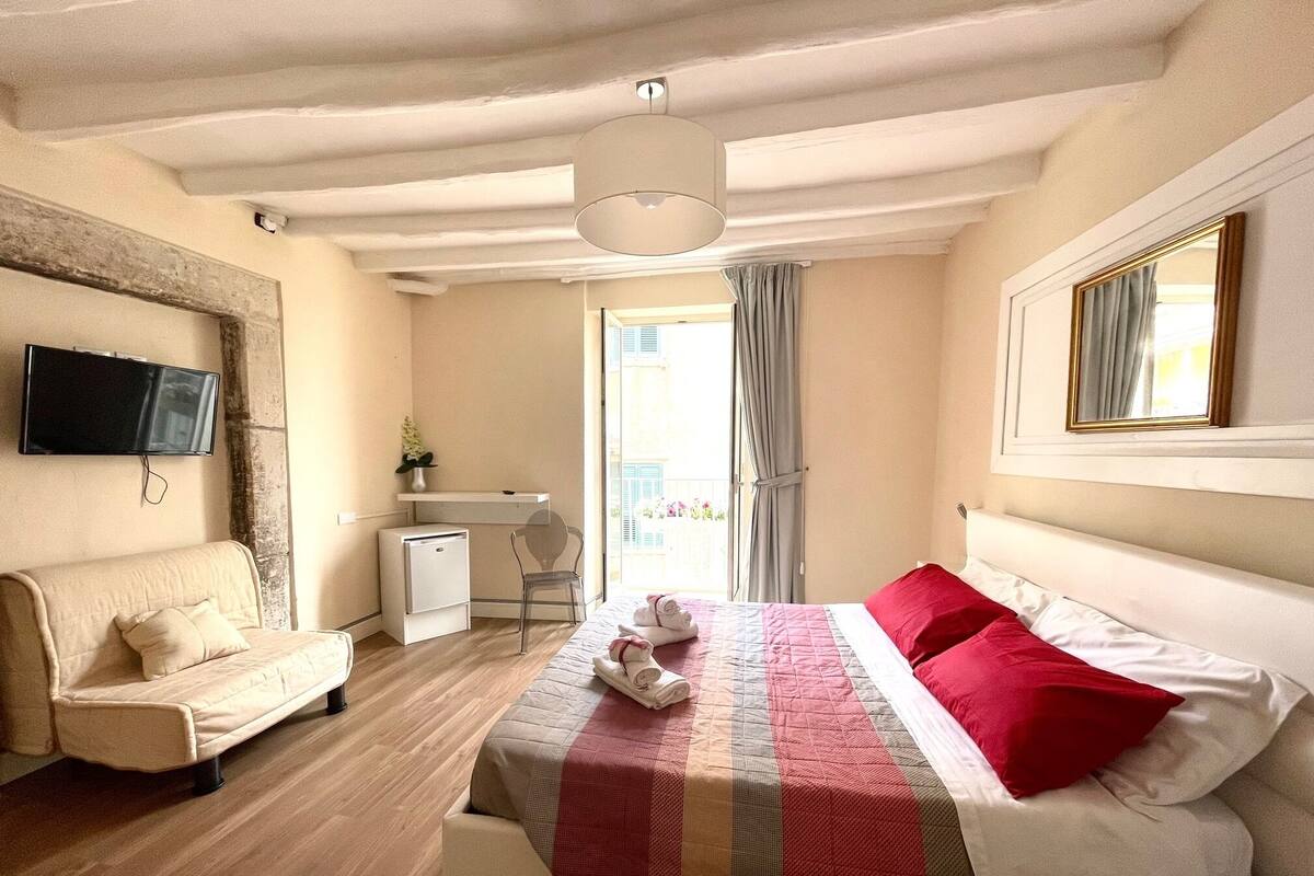 Een hotelkamer met een bed, een bureau, een stoel, een televisie en een raam met gordijnen.