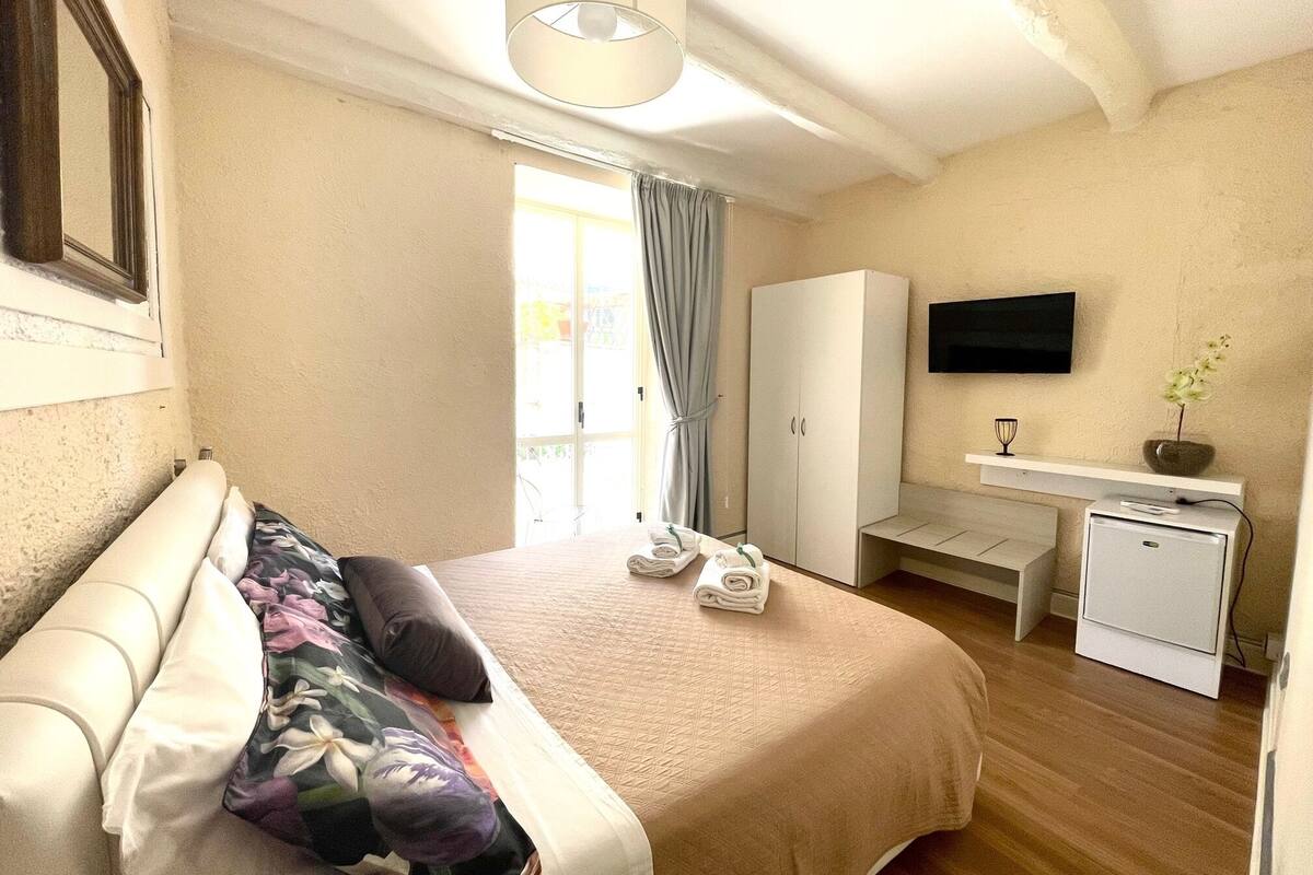 Een slaapkamer met een bed, een bureau, een kledingkast, een televisie en een kleine koelkast.