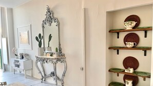 A dining area with a table, chairs, a mirror, and a wall-mounted shelf with plates and a teapot. - Residenza Donna Peppina Tropea (Tropea)