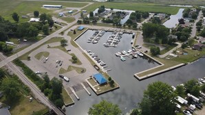 Vue aérienne d’une marina avec des bateaux amarrés, un parking et un pont reliant la marina à un quartier résidentiel.