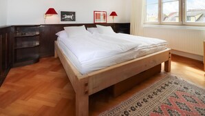 A neatly made bed in a room with a wooden floor, a patterned rug, and two wall-mounted lamps. - Ferienhaus mit Garten (Weissenkirchen in der W)