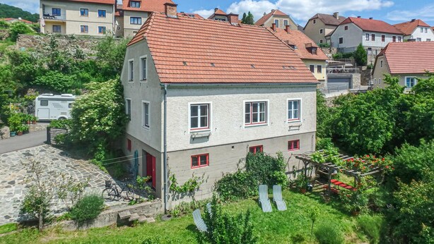 A two-story building with a red-tiled roof, a stone staircase, and a garden with potted plants and a bicycle. - Ferienhaus mit Garten (Weissenkirchen in der W)