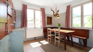 A cozy dining area with a wooden table and benches, large windows with curtains, and a rustic decor including a wall-mounted light fixture. - Ferienhaus mit Garten (Weissenkirchen in der W)