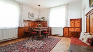 A room with a wooden dining table, two chairs, a red cushioned bench, a patterned rug, and a radiator. - Ferienhaus mit Garten (Weissenkirchen in der W)