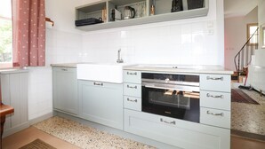 A kitchen with white cabinets, a built-in oven, and a window with a red and white checkered curtain. - Ferienhaus mit Garten (Weissenkirchen in der W)