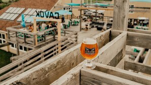 A glass of beer on a wooden bench overlooking a building with a sign that reads "CAVOK".
