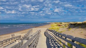 A wooden boardwalk leading to a beach with dunes and a clear sky.