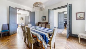 Une salle à manger avec une grande table, des chaises en osier et un luminaire suspendu.