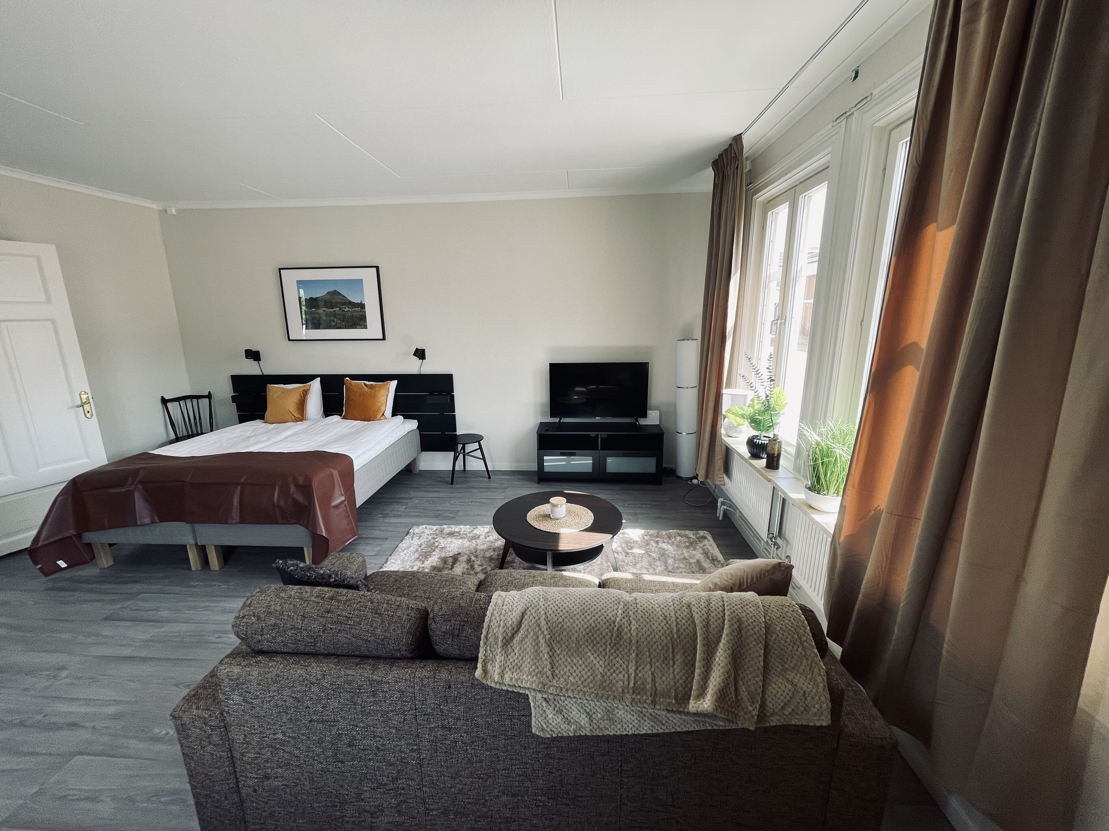 Une chambre d’hôtel avec un lit, un canapé, une télévision et une fenêtre avec des rideaux.