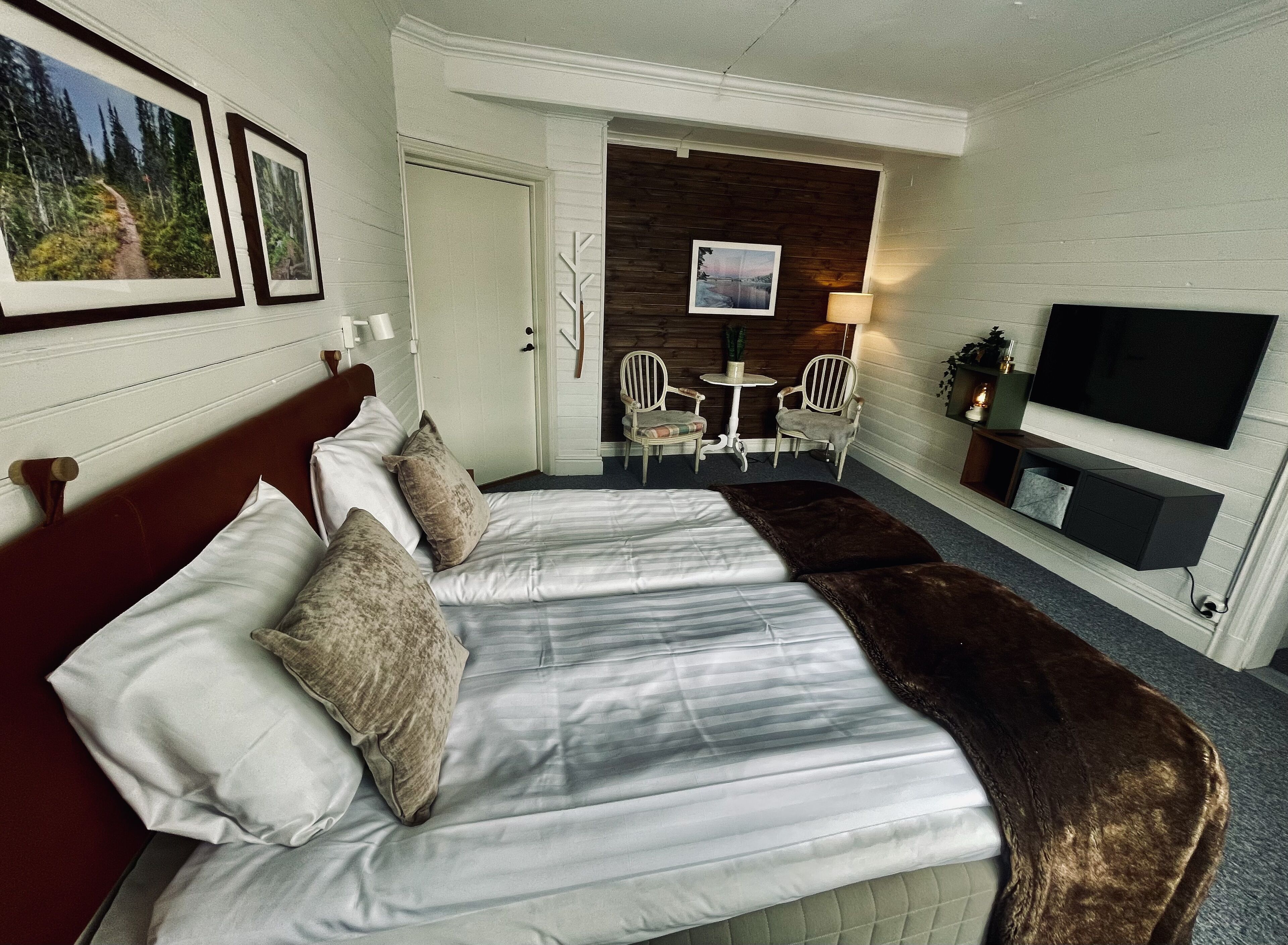 A hotel room with a large bed, a TV, a seating area with chairs, and framed pictures on the wall.