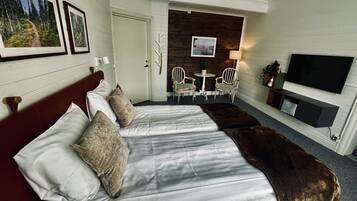 A hotel room with a large bed, a TV, a seating area with chairs, and framed pictures on the wall.