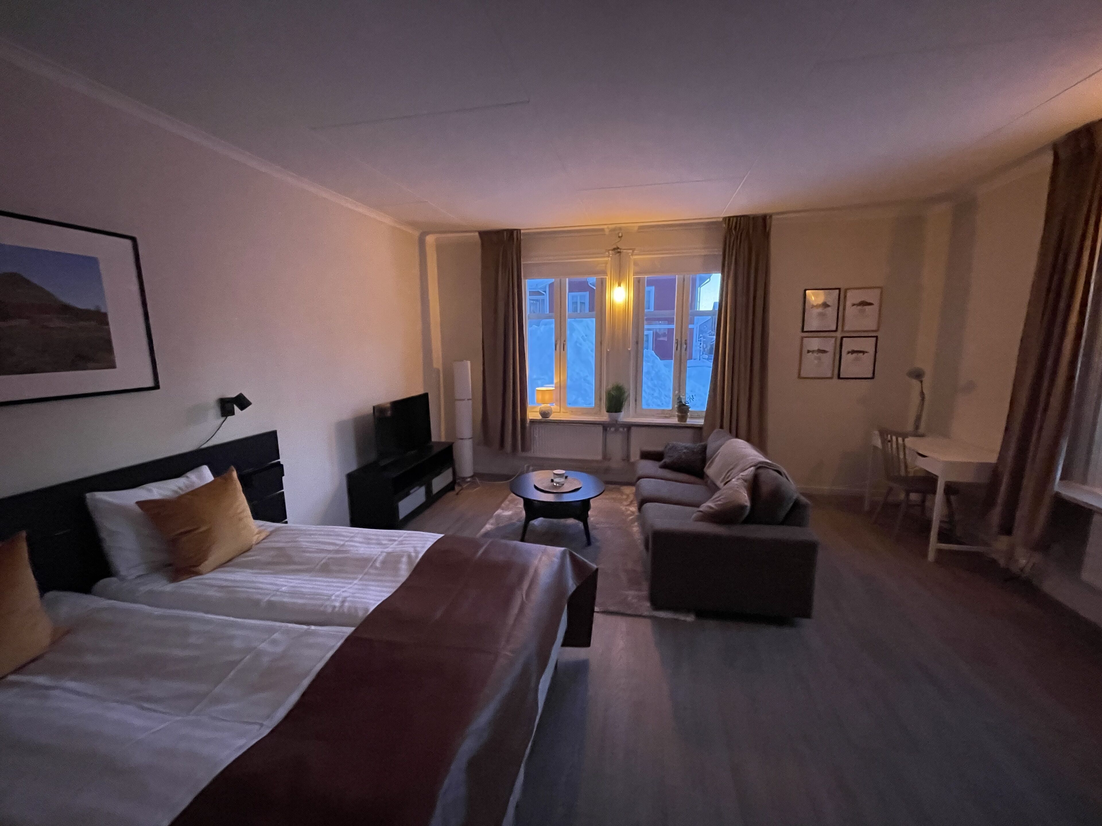 A hotel room with a bed, a sofa, a small table, and a TV.