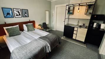 Une chambre d’hôtel comprenant un lit, un bureau, une chaise, une petite table, un lavabo et une étagère avec une plante.