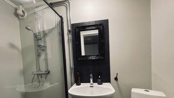 A bathroom with a glass-enclosed shower, a white sink, a black-framed mirror, and a white toilet.