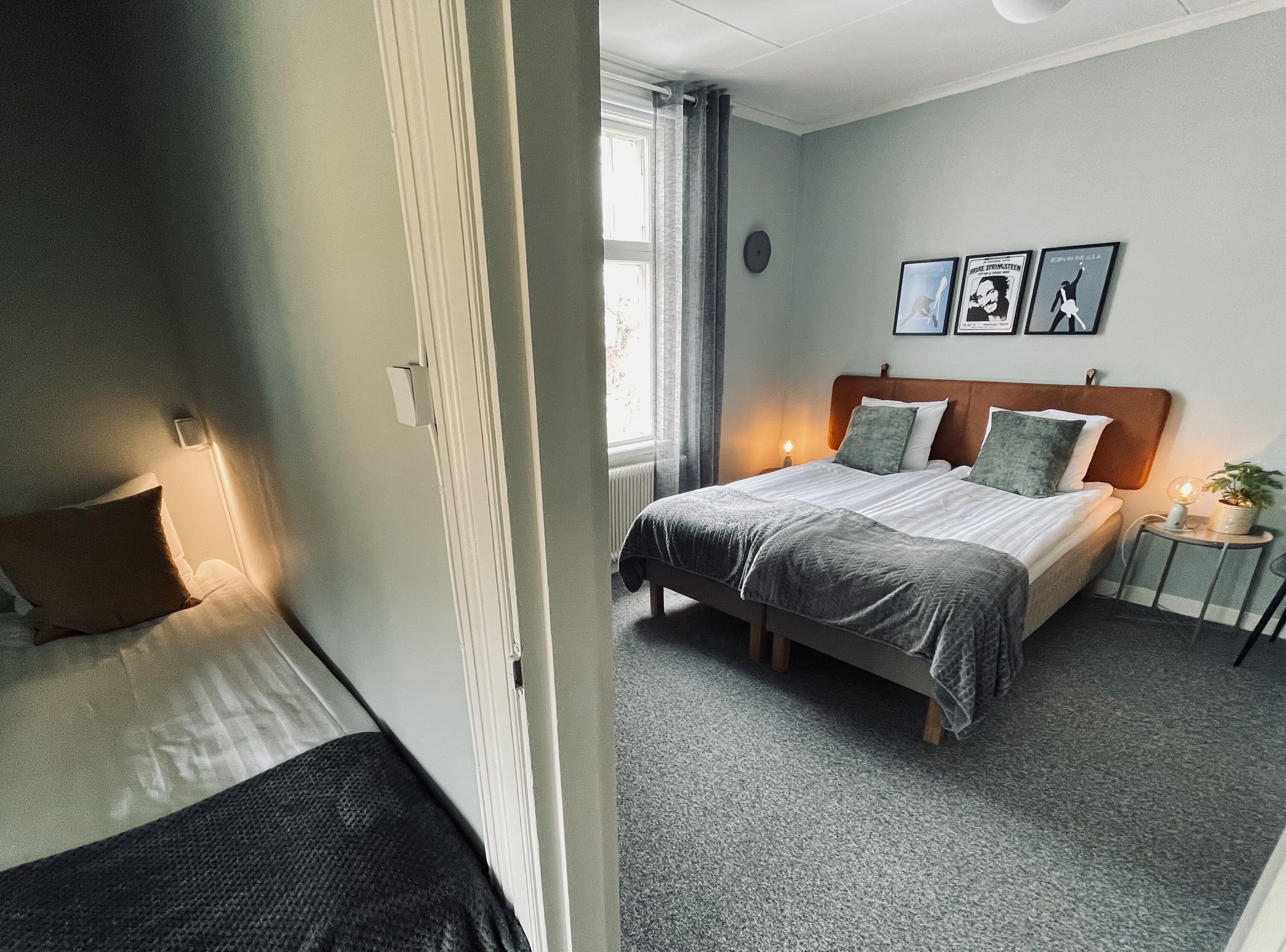 A hotel room with a bed, a bedside table with a lamp, a small potted plant, and a wall clock.