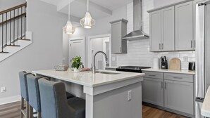 Una cocina moderna con una isla central, armarios grises, electrodomésticos de acero inoxidable e iluminación colgante.