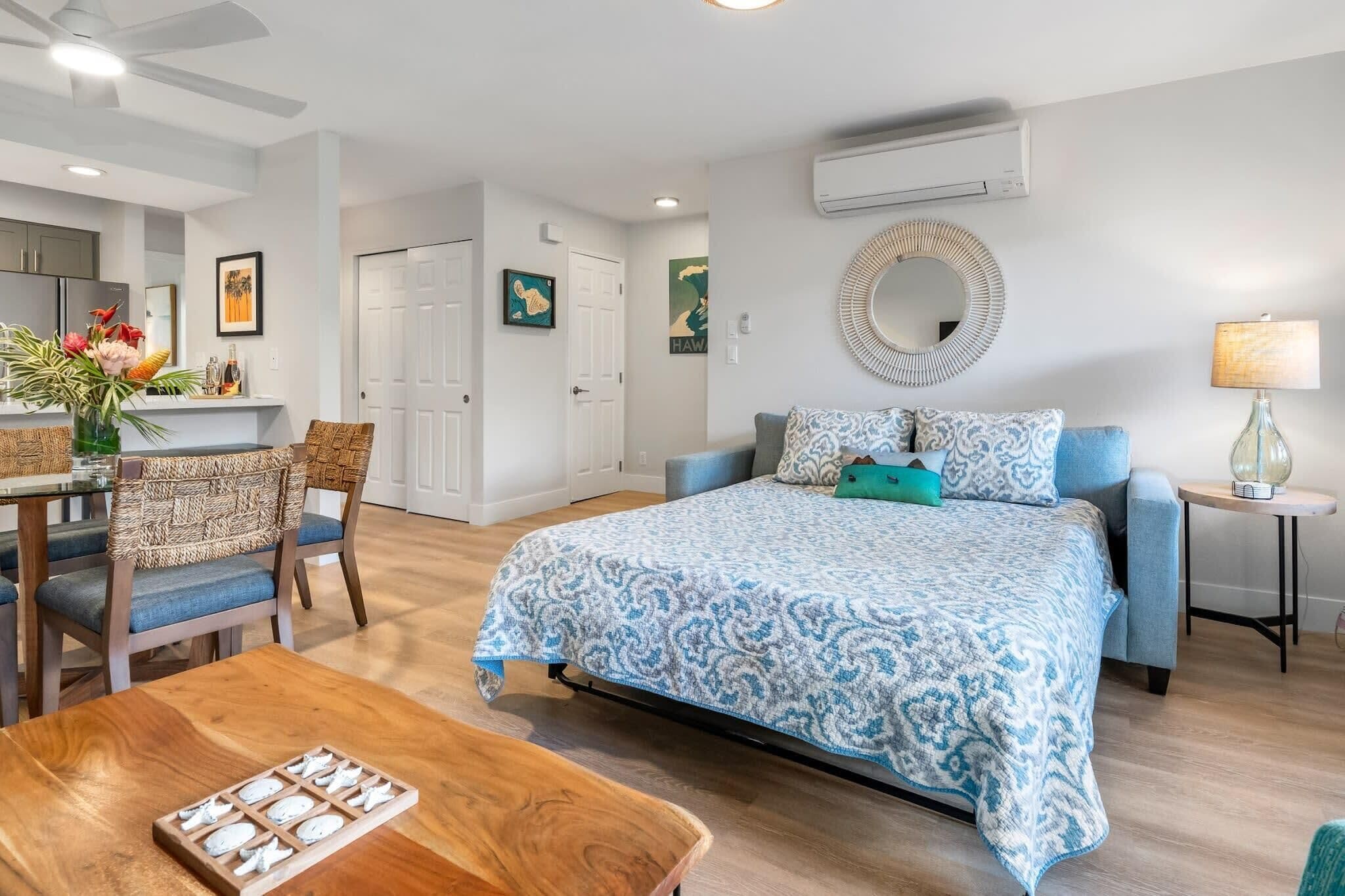 Une chambre moderne avec un grand lit, un coin repas avec des chaises en osier et une petite table agrémentée d’un élément décoratif.
