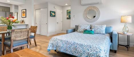 Une chambre moderne avec un grand lit, un coin repas avec des chaises en osier et une petite table agrémentée d’un élément décoratif.