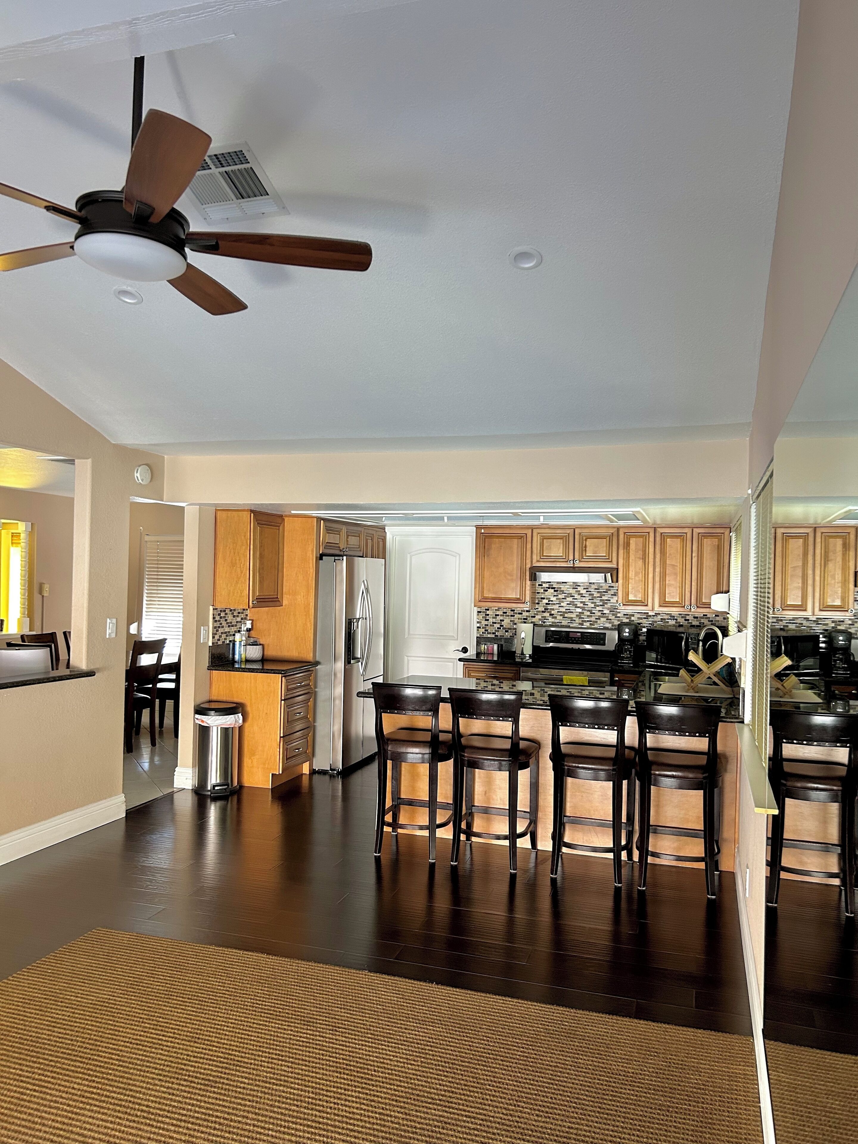 A spacious kitchen with dark wood cabinets, a central island with bar stools, a ceiling fan, and a view into the dining area.