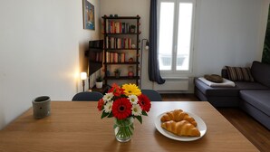 A living room with a wooden table, a bookshelf, a sofa, and a window with curtains. - Montmartre & Eiffel Tower View – In the Heart of Authentic Paris (Paris)