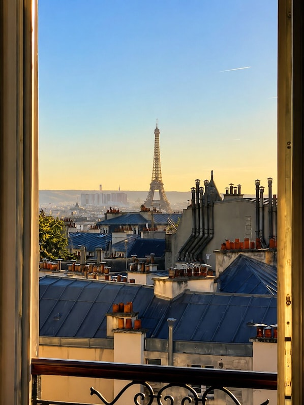 Vista de la Torre Eiffel desde una ventana con vistas a un paisaje urbano de tejados y edificios.