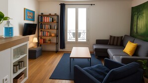 A modern living room with a sofa, armchairs, a coffee table, a bookshelf, a TV, and a large window with curtains. - Montmartre & Eiffel Tower View – In the Heart of Authentic Paris (Paris)