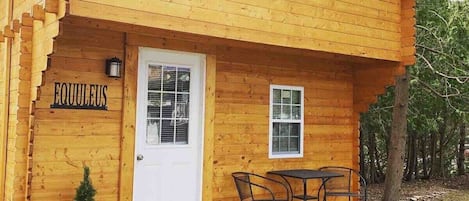 A wooden cabin with a white door, two windows, a small porch with a table and chairs, and a sign that reads "EQUULEUS".