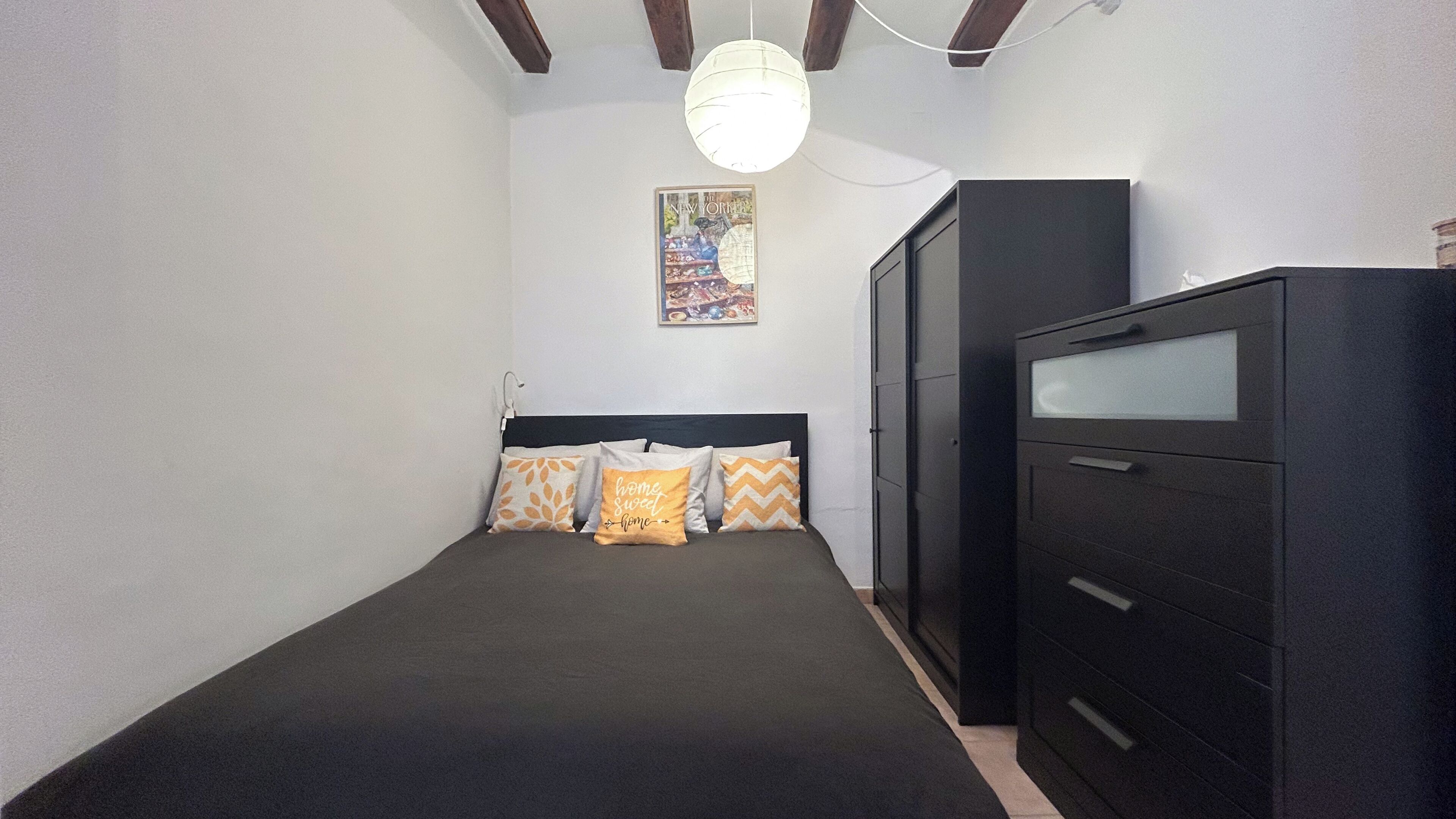 Une chambre à coucher comprenant un lit, une commode et un luminaire fixé au mur.