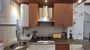 Una cocina con armarios de madera, un lavamanos de acero inoxidable, una estufa a gas y una campana extractora.
