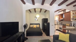Ein kompakter Wohnraum mit Bett, Fernseher, Ventilator, Sofa und einer Küchenzeile.