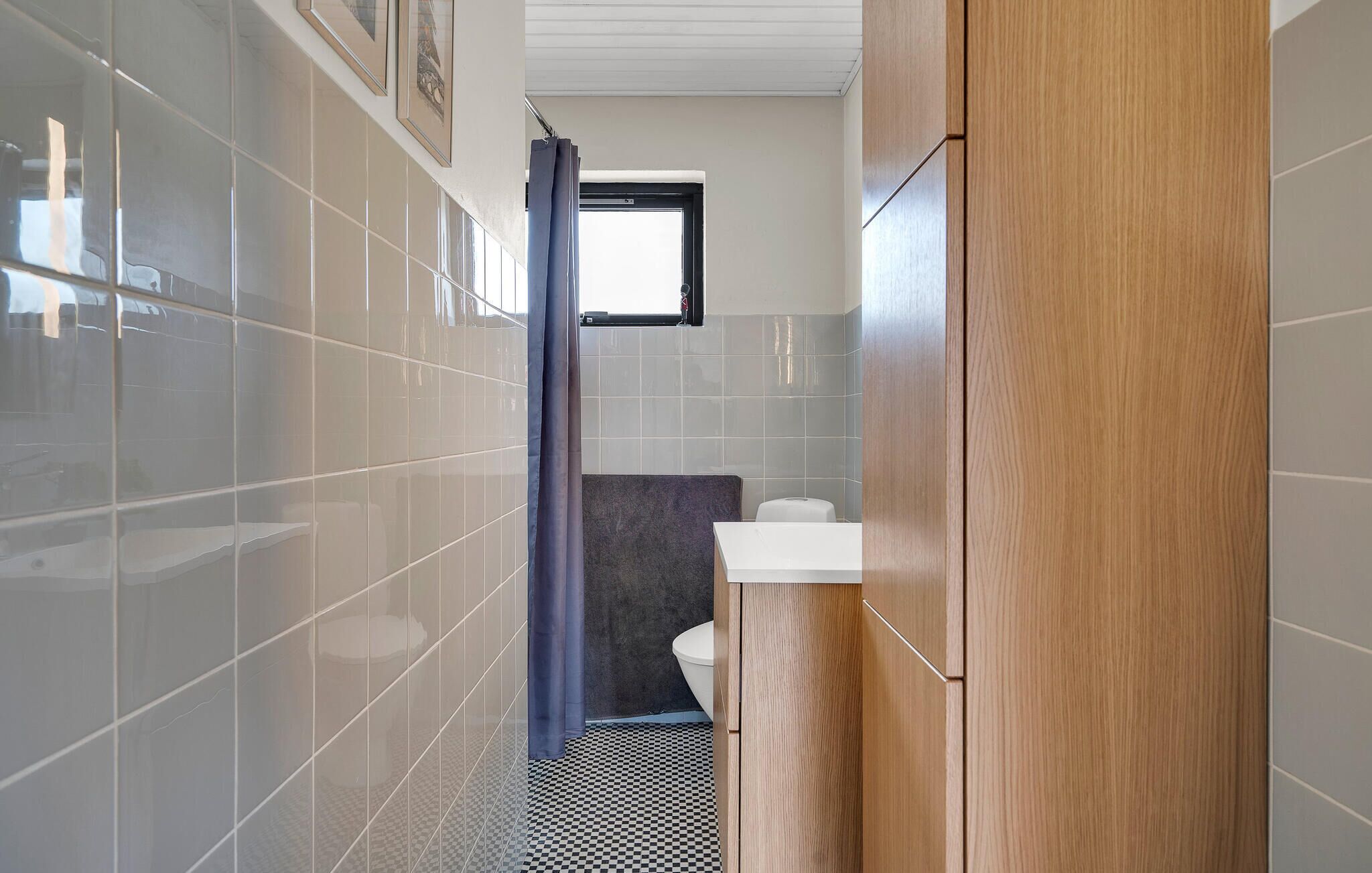 A narrow bathroom with tiled walls, a checkered floor, a wooden cabinet, and a toilet.