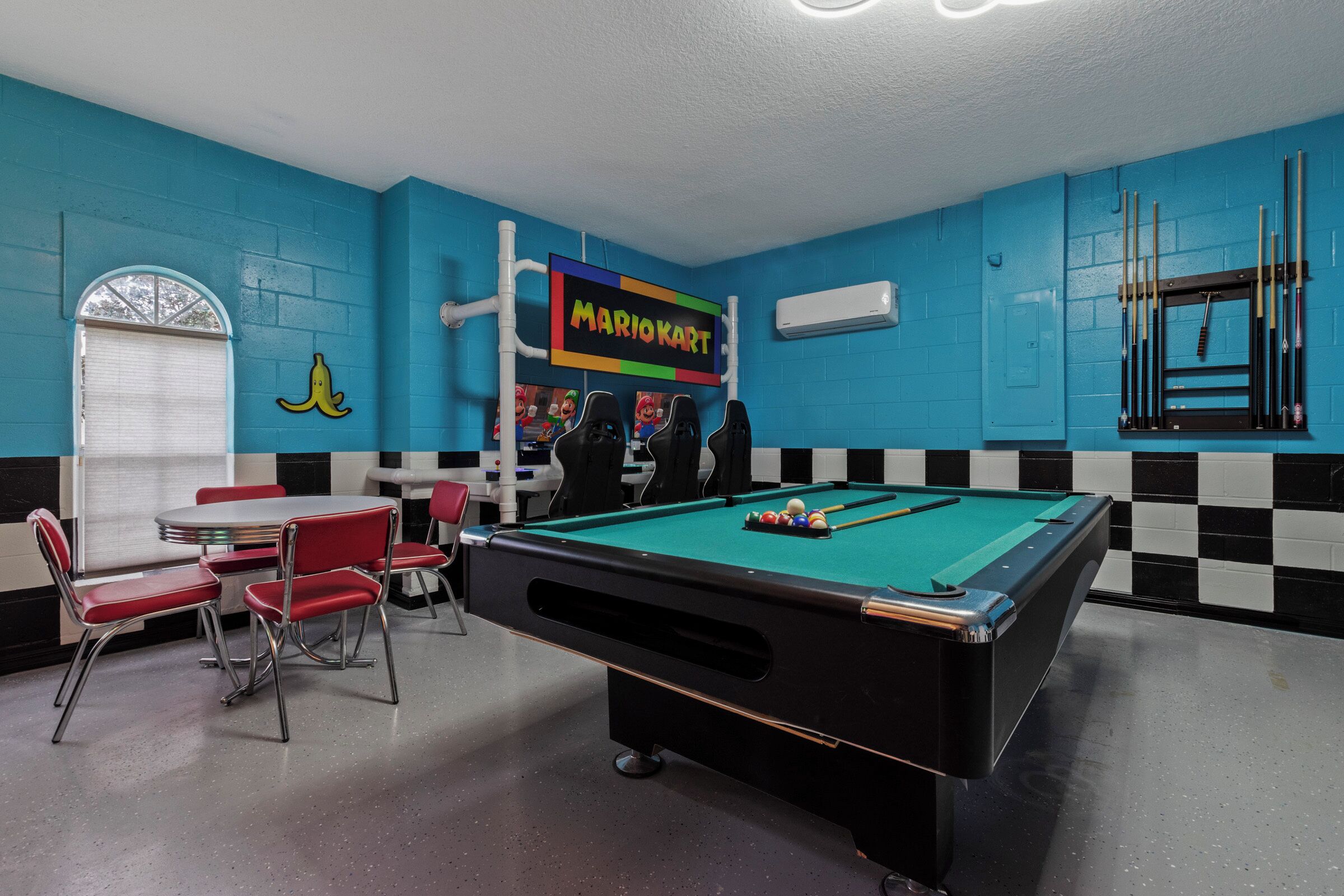 A pool table with a Mario Kart sign, red chairs, and a checkered wall pattern.