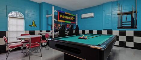 A pool table with a Mario Kart sign, red chairs, and a checkered wall pattern.