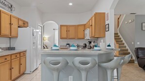 Una cocina moderna con armarios de madera, un refrigerador blanco, un microondas y una barra con taburetes.