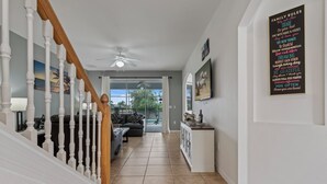 Un interior moderno con una escalera, una sala de estar con sofá y mesa de centro, y una cocina con encimera y refrigerador.