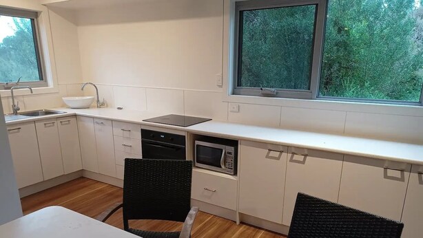 Une cuisine de taille réduite avec des meubles blancs, un évier, une cuisinière et un four à micro-ondes. On y trouve deux chaises noires et une table blanche.