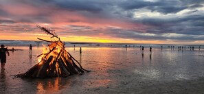 A beach scene with a campfire and people walking along the shore.