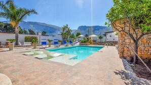 A swimming pool with lounge chairs and umbrellas, surrounded by stone walls and plants. - Nice home in Terrasini (Terrasini)